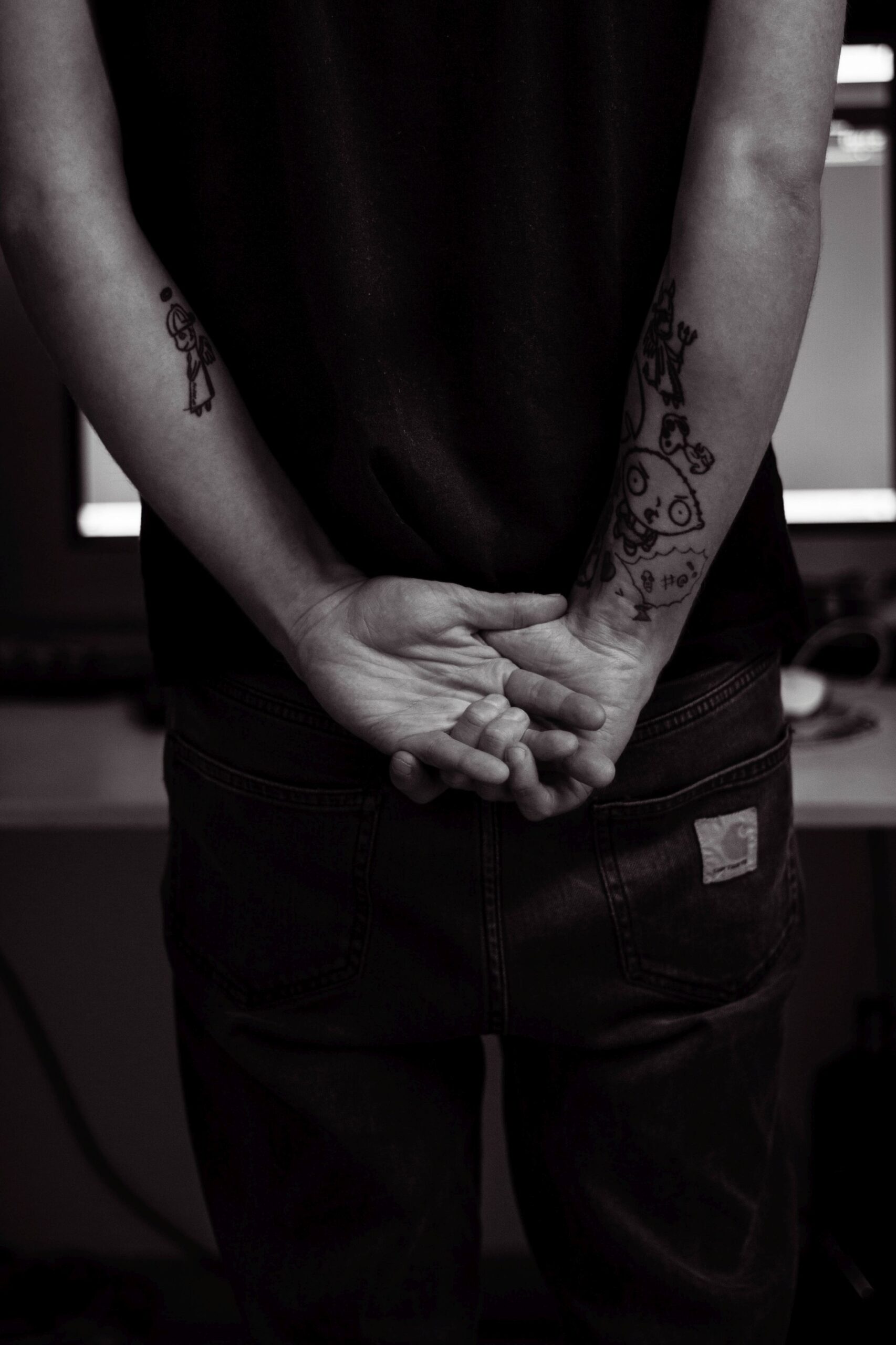 Zu sehen sind nur der Rücken und die Hände von Rapper Adrinalin. Er hat die Hände nach hinten ausgestreckt und hinterm Rücken zusammengeführt. Sind sind ineinander verschlungen.