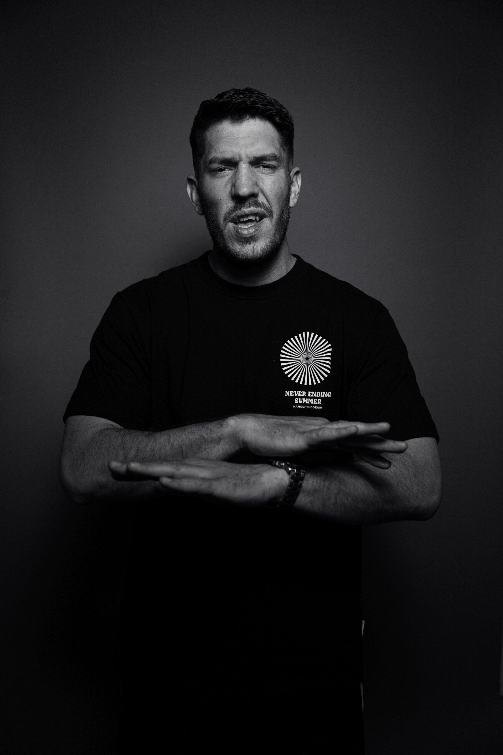 Rapper Inkasso auch Oberhausen rappt vor der Kamera. Er hat beide Arme gebeugt und die Handflächen gerade ausgestreckt. Die Arme überkreuzen sich in der Pose. Man sieht, dass der Rapper gerade singt. Das von Foto wurde von Fotograf Toni Borgert aufgenommen.