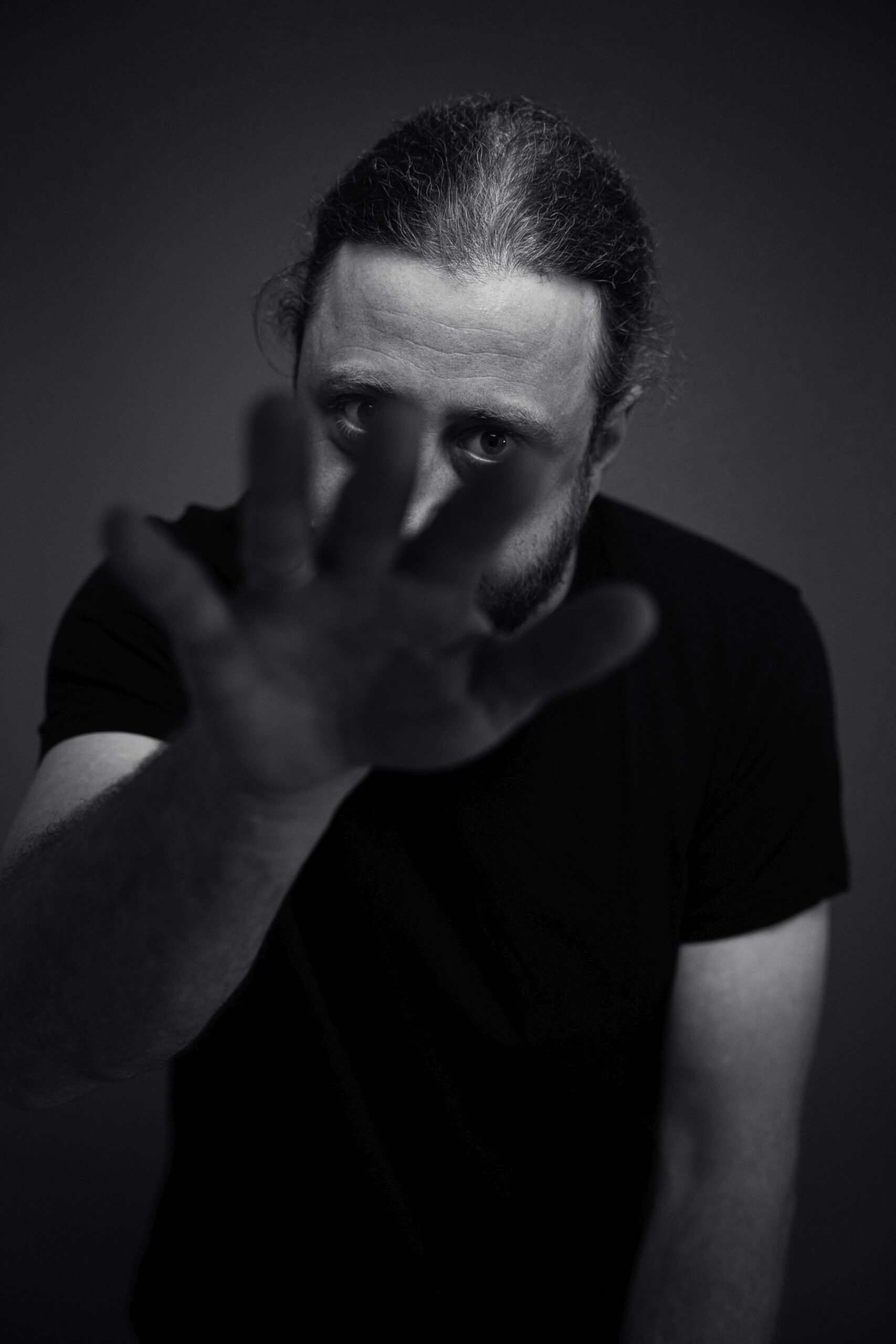 Das Foto zeigt den Rapper Keeko aus dem Ruhrgebiet in NRW. Auf dem Bild rappt er ein Lied und hat eine Hand in Richtung Kamera ausgestreckt. Durch die ausgestreckten Finger kann man seine Augen scharf erkennen. Der Rest des Bild ist eher unscharf. Keeko steht vor einem dunklen Papierhintergrund und trägt ein schwarzes T-Shirt. Das Foto wurde von Fotograf Toni Borgert aufgenommen.