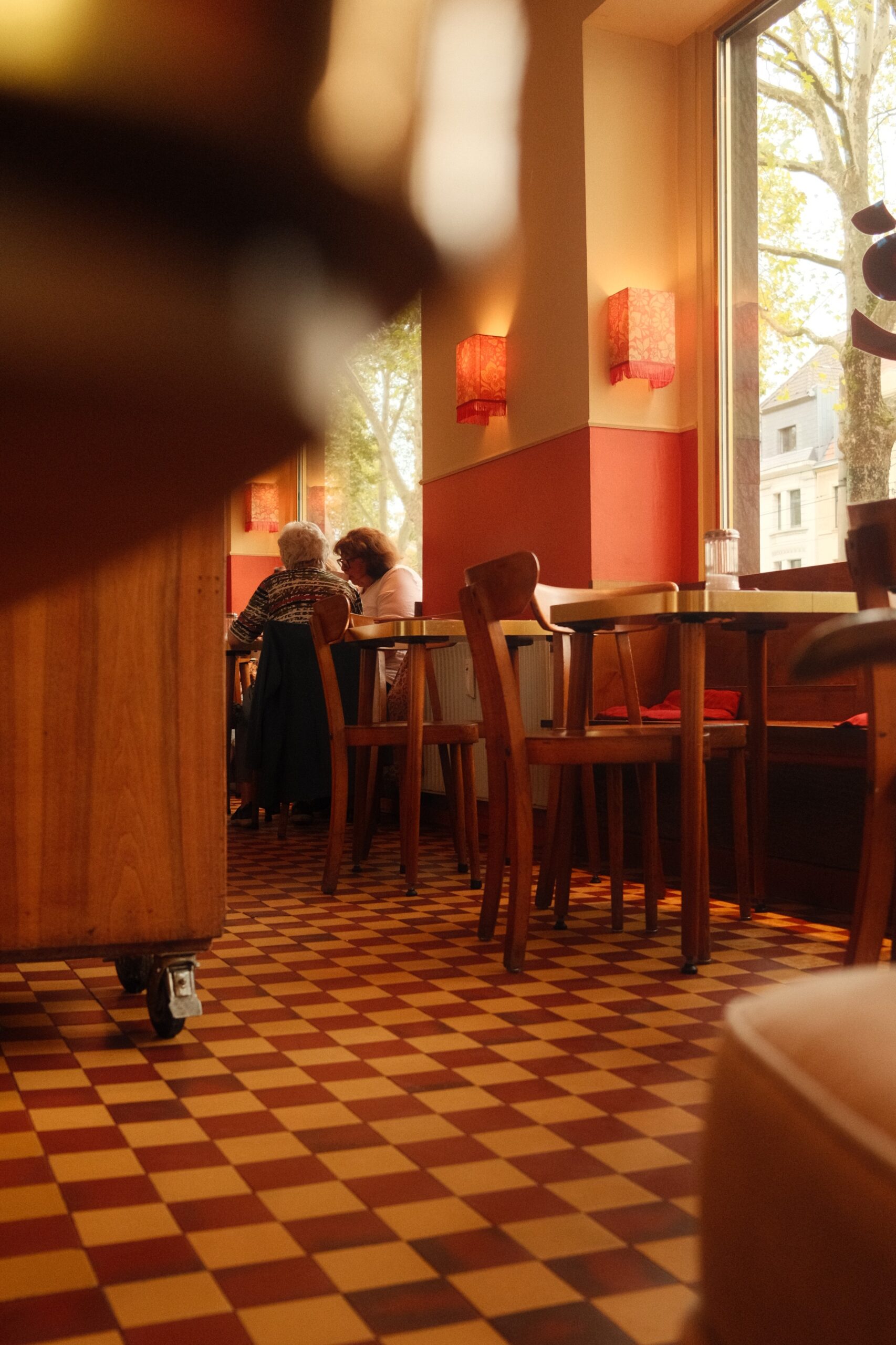 Koeln_CafeFranck_innen©TBorgert Das Foto zeigt das Café Franck in Köln von innen. Im Hintergrund sitzen zwei Personen am Tisch. Daneben ist ein weiterer Tisch zu erkennen. Im Vordergrund sieht man den fliesten Fußbodem im Schachbrettmuster und typisch im Stil der 1950er Jahre. Das Foto wurde von Fotograf Toni Borgert aufgenommen.